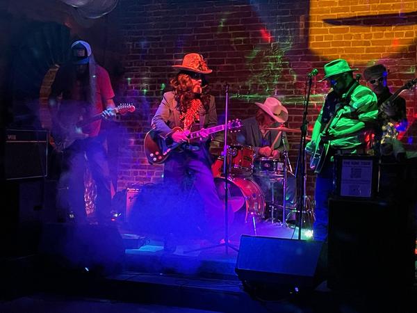 Photo of Five musicians in front of a brick wall. 