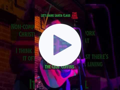 Video of an incredibly handsome man singing and playing guitar at a microphone. The title Let's Hang Santa Claus and the logo The King Teen appear, as do lyrics as they're sung. 