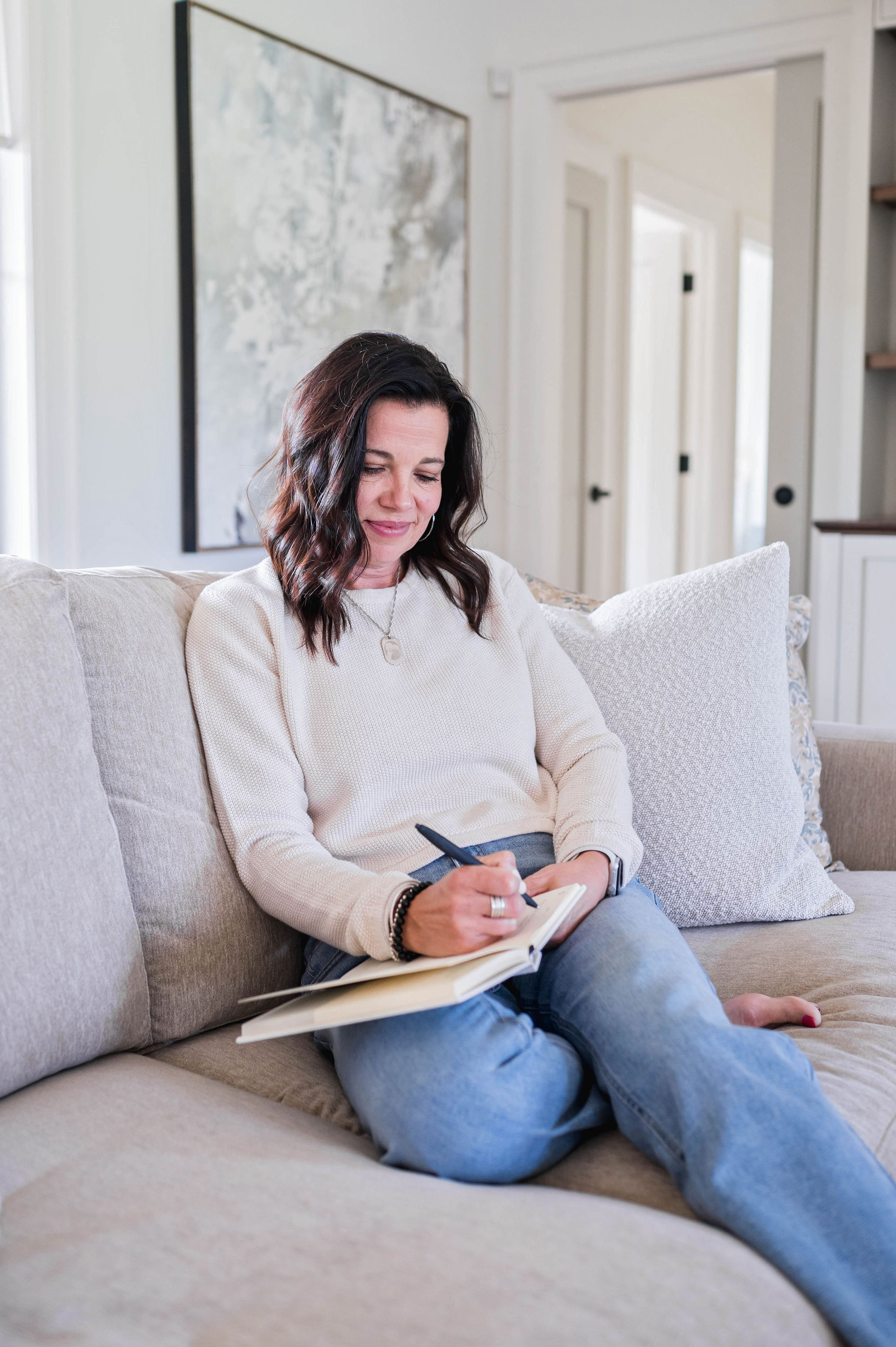 Andrea Bowen, holistic nutritionist, writing in a journal on a cozy couch