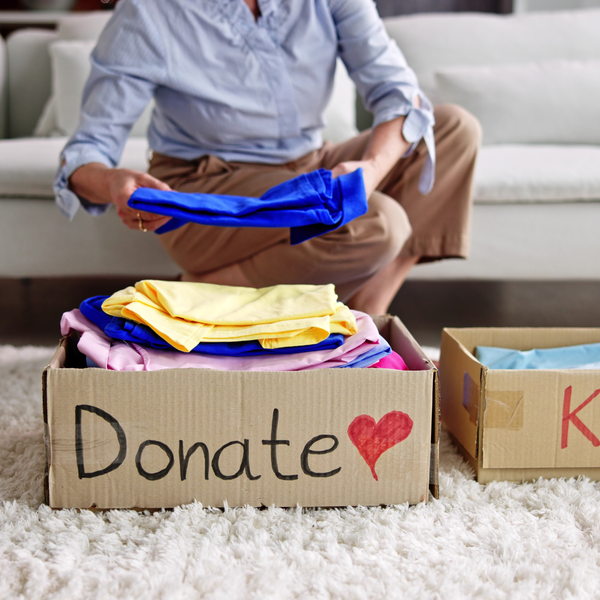 A woman placing a blue shirt in a box labled "Donate" rather than the "Keep" box to the right of it.