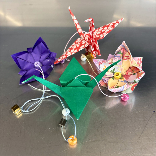 Various origami creations attached by a string running through each one with various beads lays on a metal counter.