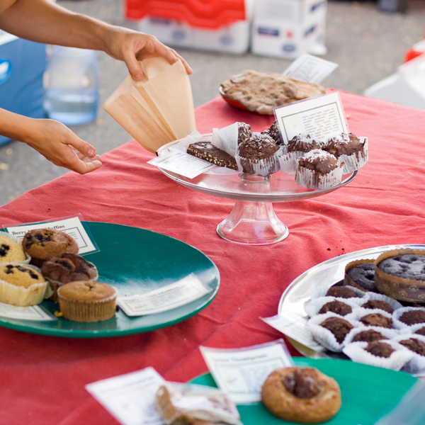 Various baked goods across a table. Someone is packaging baked goods.