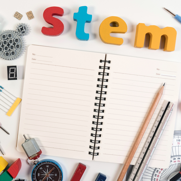 Various STEM items are scattered throughout with a notebook in the middle and the foam words spelling "STEM" out on top.