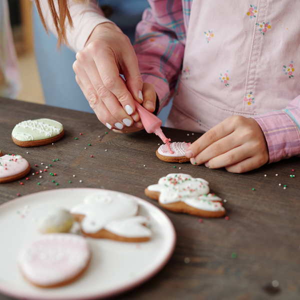 A girl decorating a sugar cookie with pink icing.