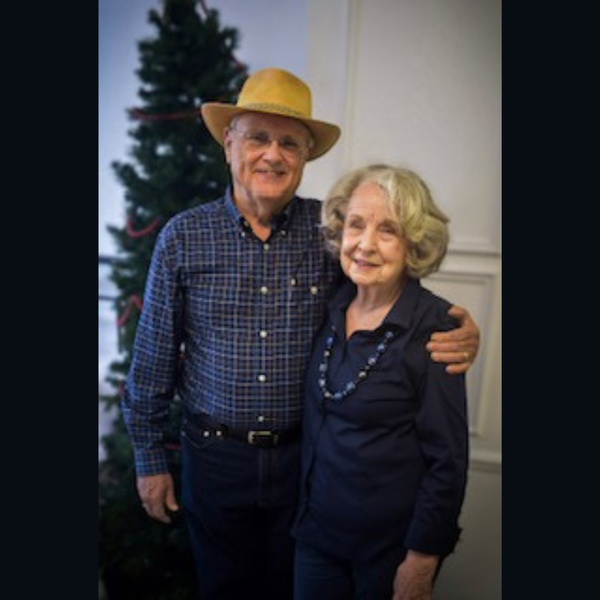 A man and woman imbracing each other with a tree in the background.