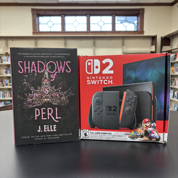 A black book bedazzled with pink rhinestones is on the left while the box of the library's Nintendo Switch 2 is on the right side on a tall, black table.