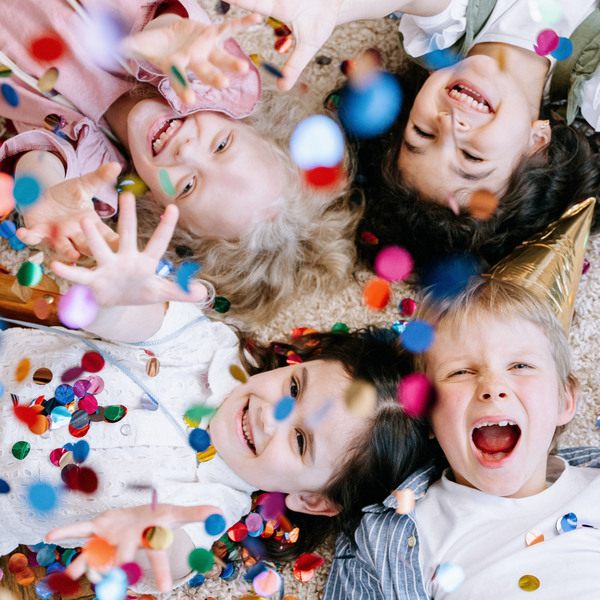 Children laying on the ground reaching up trying to catch confetti.