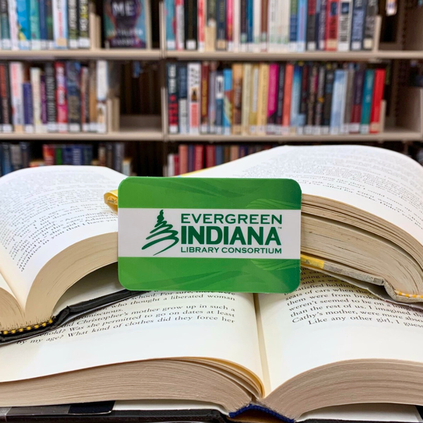 A green Evergreen library card propped up against a pile of books in the background.