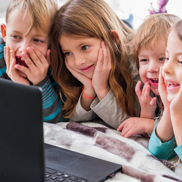 Four young children laying down, crowding around a laptop to watch whatever is playing on it.