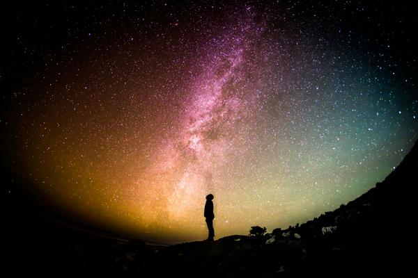 Silhouetted image of a person looking up at the Milky Way in vast, starlit night sky.