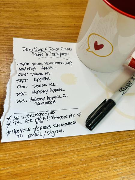 Image of Lisa Sargent's desk with a coffee mug and notepaper. On the notepaper is a listing of a sample donor communications calendar for one year. 