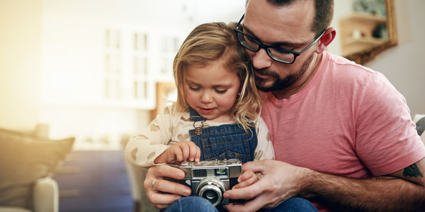 A man sitting with a young girl examining the buttons on a camera.