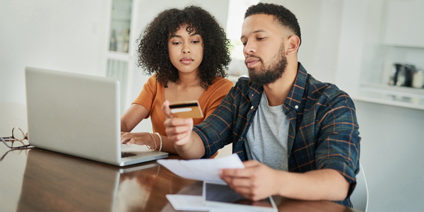 A man and a woman looking at a credit card while sitting in front of a laptop