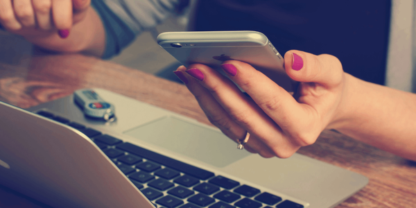 A woman holding a mobile phone above a laptop