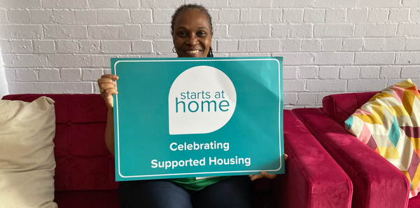 An ISHA staff member sitting on a sofa holding a 'Starts at home' campaign poster