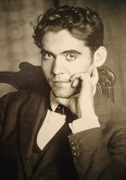 A black-and-white portrait of a seated person in a dark suit, high-collared white shirt, and bow tie, resting their head thoughtfully on one hand.