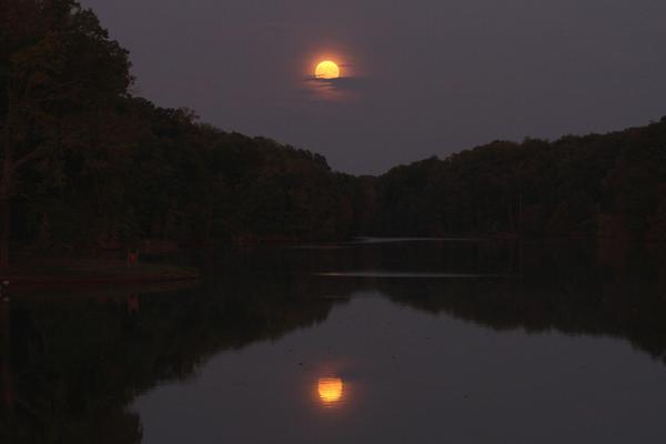 Moon rising over a dark lake and reflected in the water