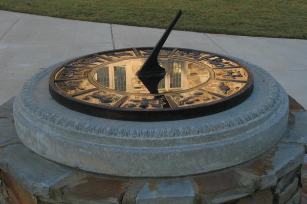 Sundial with reflective surface mounted on round cement pedestal.