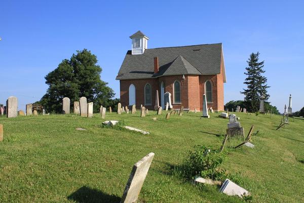 A brick church surrounded by headstones of an old cemetery.