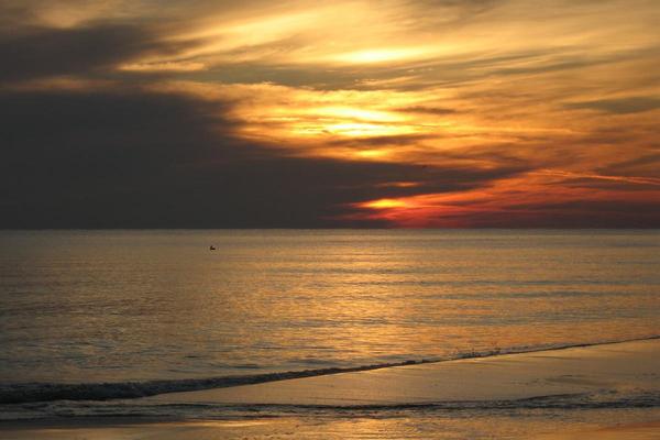 Orange sunset sky with dark clouds to the left and orange reflections on water in the foreground.