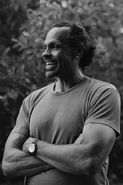Portrait of a African American woman smiling broadly with a colorful necklace and standing in front of a background of green foliage.