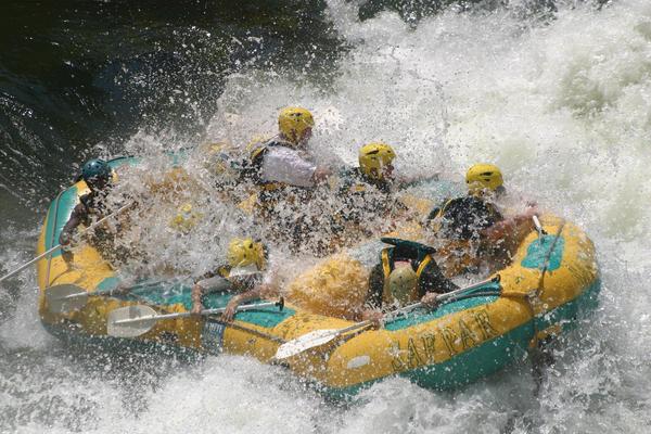 Inflatable raft with helmeted passengers in white water river