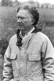 Black and white photo of May Sarton standing with her elbow leaning against the wall.