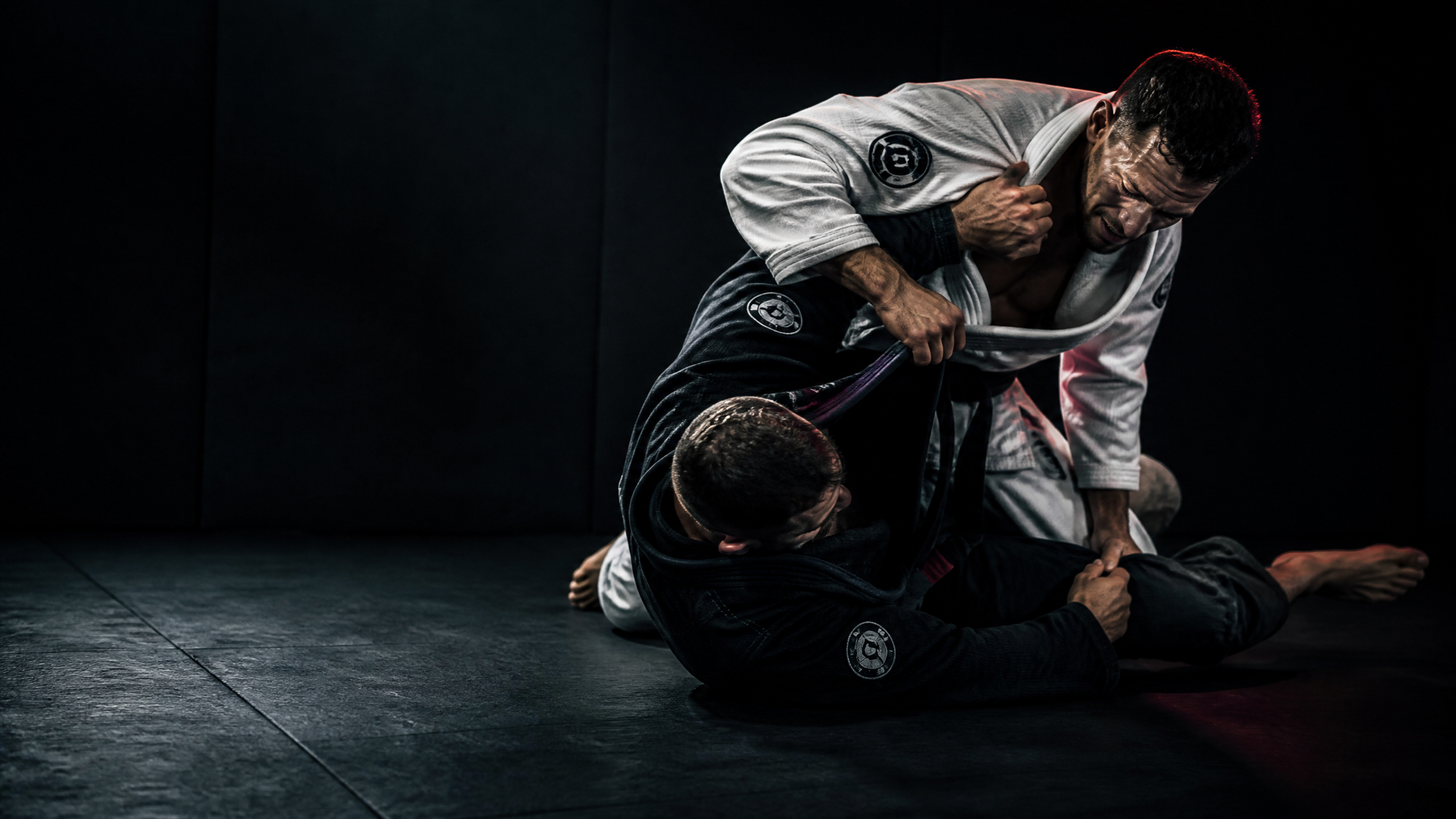 Two male grapplers training on a dark mat