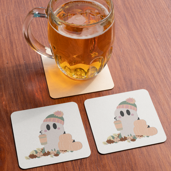 A glass of amber beer on a coaster beside two more coasters featuring a cute ghost in a beanie, holding coffee amidst autumn leaves and pumpkins. Cozy, fall theme.