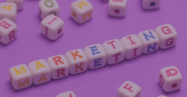 White dice with colorful letters spell "Marketing" twice on a purple background. Scatter dice surround them, creating a playful and creative vibe.