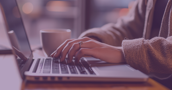 Woman typing on a laptop in a coffee shop, representing why businesses should maintain a blog on their website