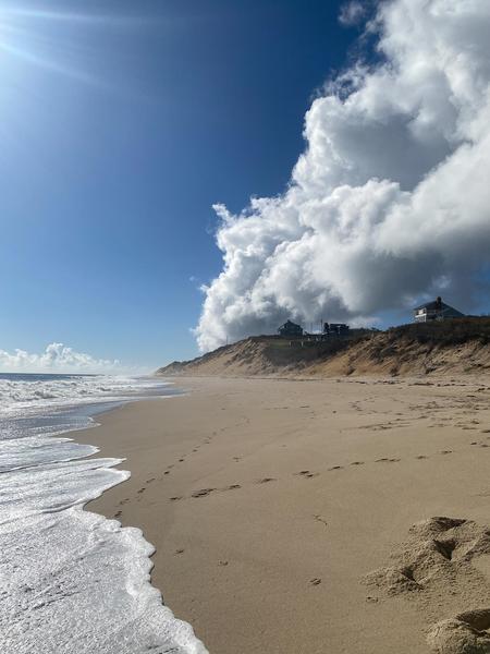 ebullient white clouds hover over a sun-lit cliff home, with a starburst in the sky, and white frothy waves inspiring power