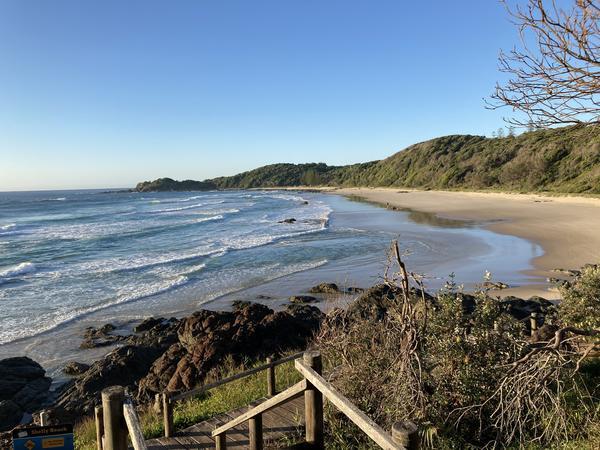 A photo of small waves breaking onto a long stretch of sandy beach, flanked by a forested hillside