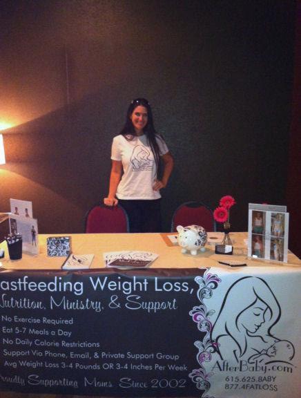 Amber at her AfterBaby booth at the Trust Birth convention, among doulas, midwives and birthing professionals, with her banner: Breastfeeding Weight Loss, Nutrition, Ministry & Support
