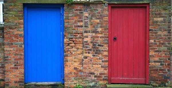 Two doors, a blue one on the left and a red door on the right on brick walls