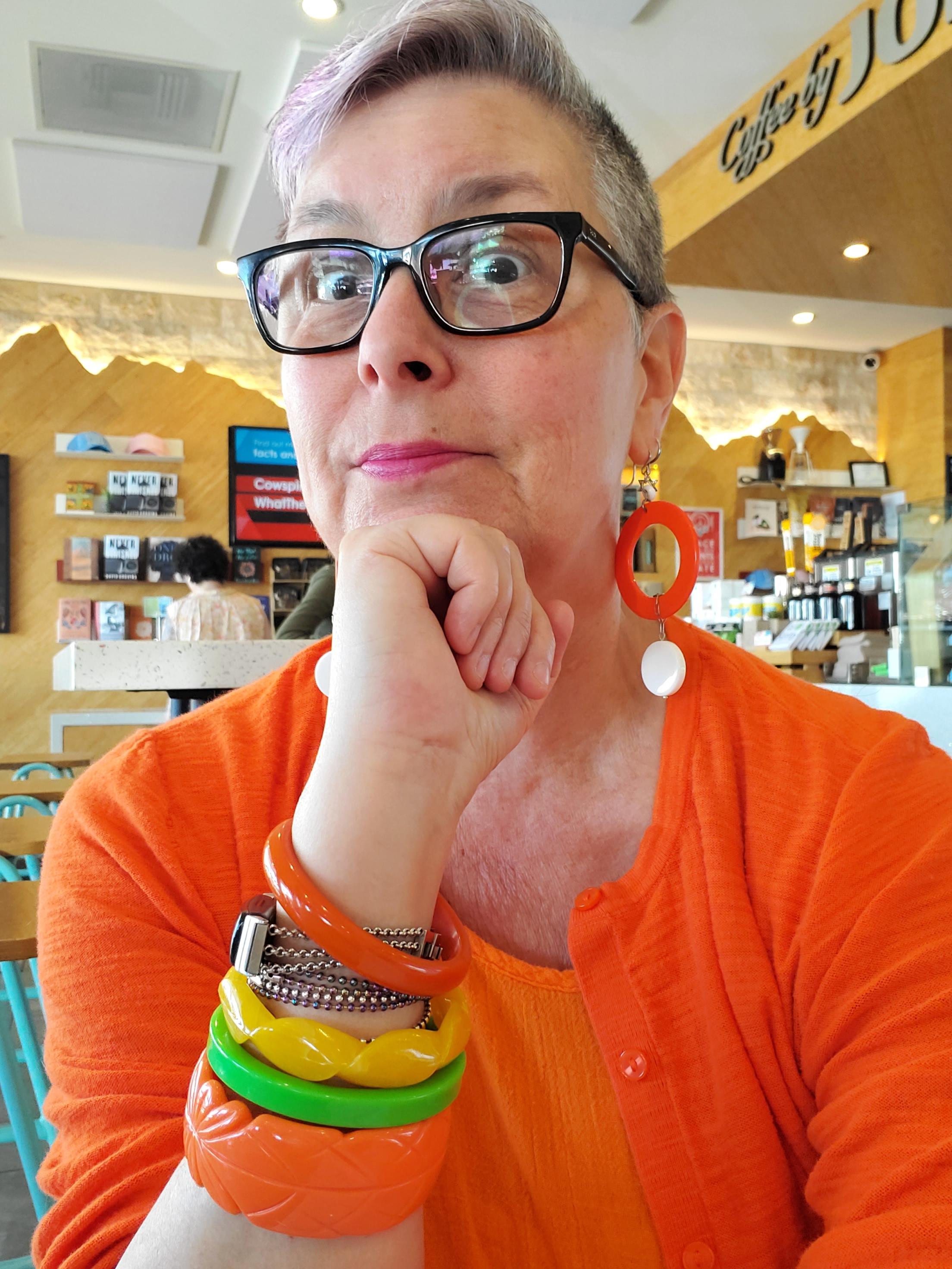 Picture of Lisa in an orange sweater, orange earrings, and orange, green and yellow bracelets.