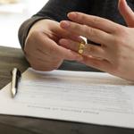 A person signing papers and removing a wedding ring