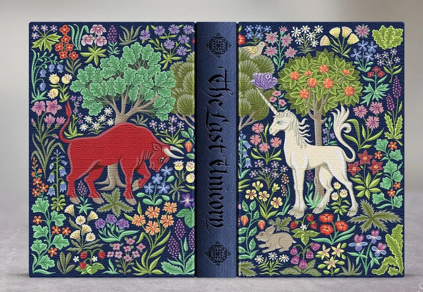 The Last Unicorn from Suntup Editions: deep blue binding with an embroidered millefleur design of a red bull and a white unicorn among flowers and trees, with the title in blackletter on the spine