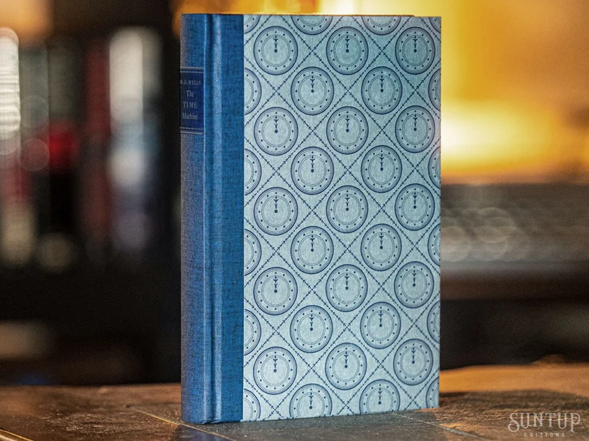 The Time Machine from Suntup Editions: blue cloth spine with a title label and patterned boards printed with a repeating clock-face motif, standing upright