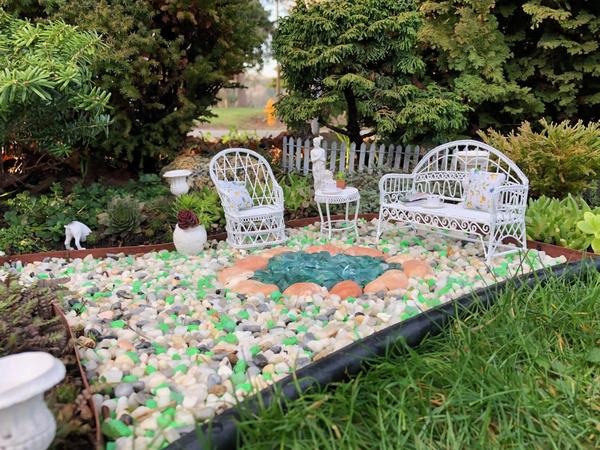 An inground miniature garden with white wicker furniture