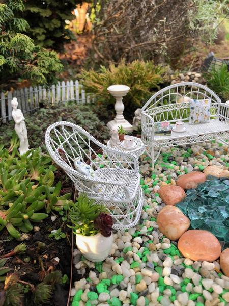An inground miniature garden with white wicker furniture