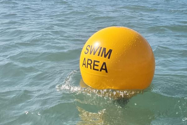 A yellow buoy in the sea with the words SWIM AREA