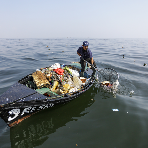 A man on a small boat using a fishing net to remove plastic from the ocean