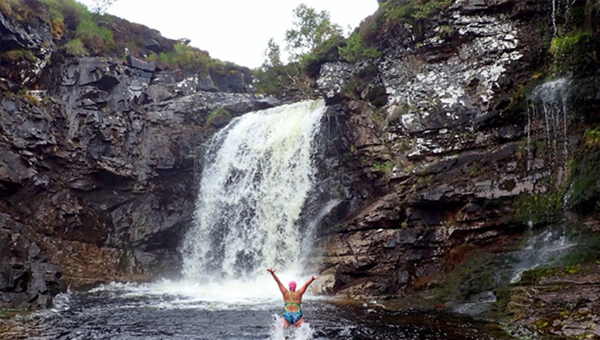 Swimmer with arms in the air in front of waterfall