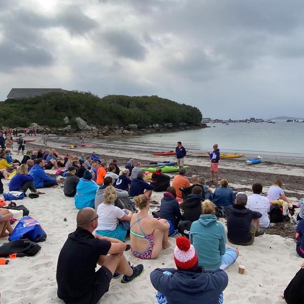 People sitting on a beach looking towards the sea during a pre-swim briefing