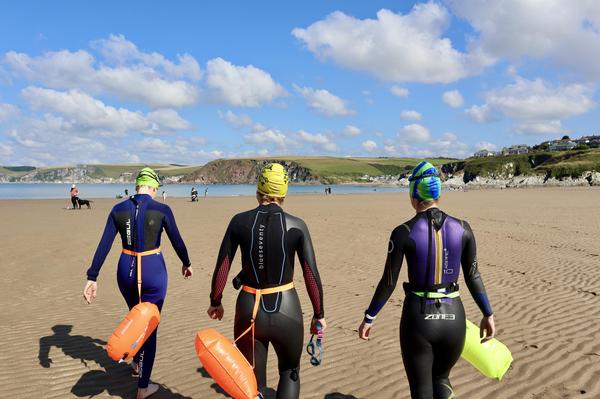 Three swimmers approaching sea on beach