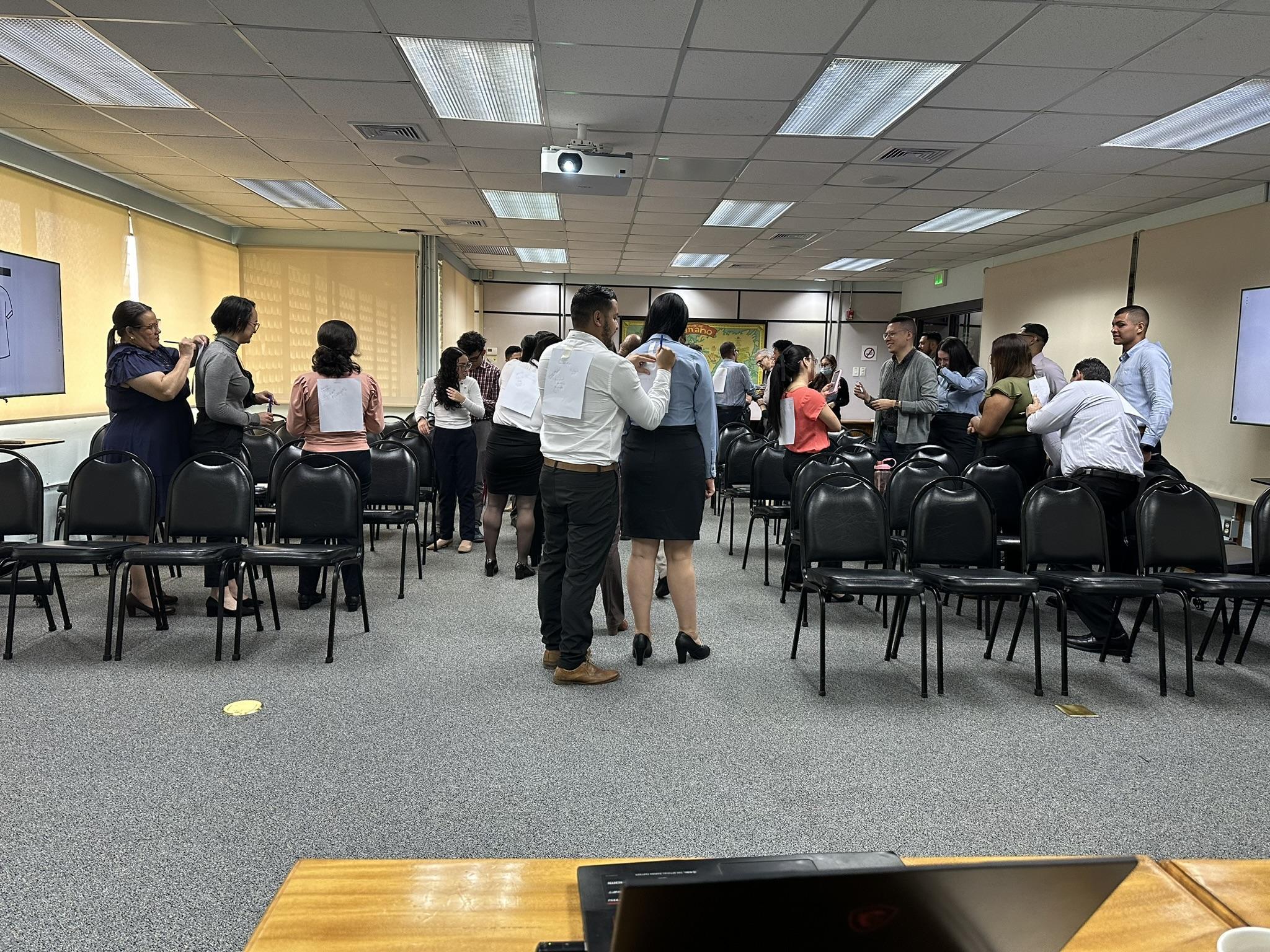 Participantes realizando una dinámica grupal, escribiendo en hojas pegadas en la espalda de sus compañeros