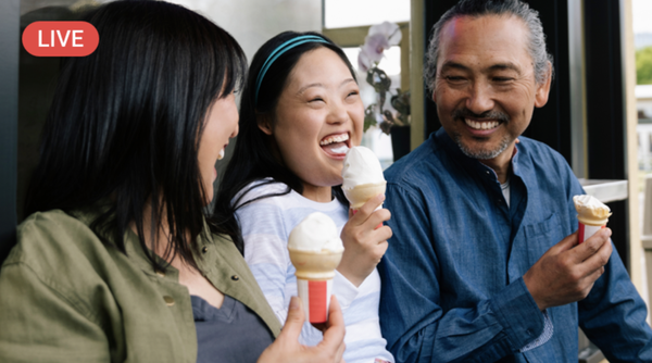 An image of a family of three with a man with greyish hair and a beard, holding an ice cream cone and smiling towards his daughter who sits right next to
him. His daughter wears a white shirt and is excited to eat her ice cream. Next to her sits her mother also looking towards her and also holding an ice cream cone. 