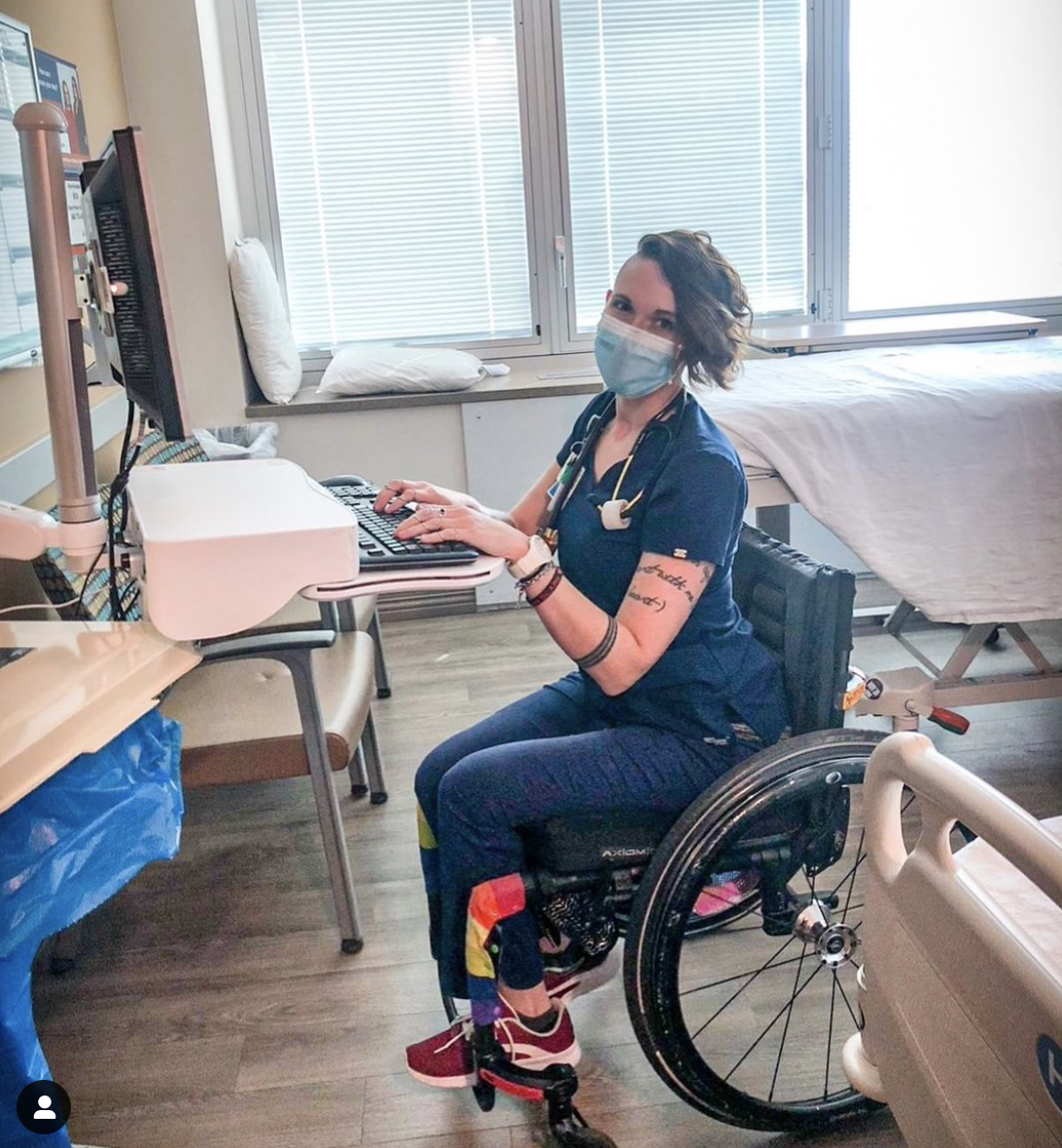 A photo of a woman in blue nurse dress and a face mask sitting in a wheelchair