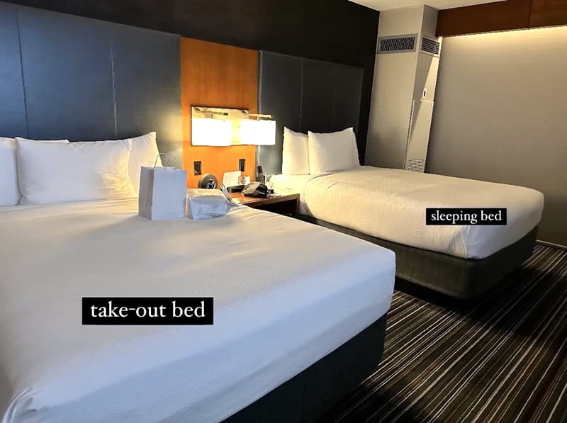 Two hotel beds, one with takeout food on it